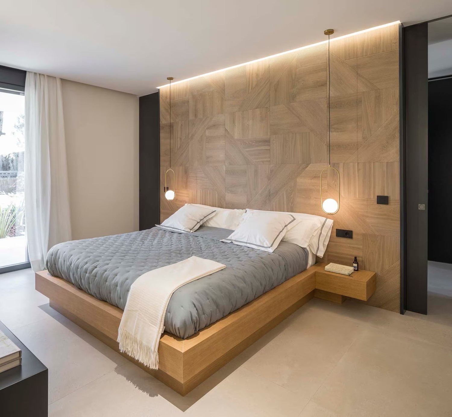 Minimalistyczna sypialnia z drewnianym łóżkiem i lampą wiszącą. fot. Porcelanosa