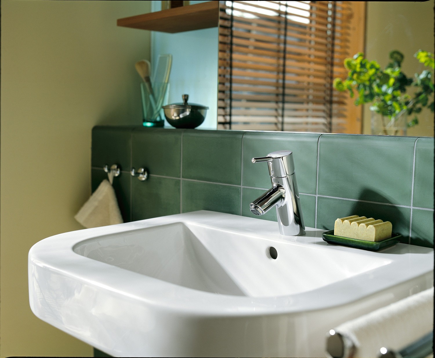 Biała umywalka z chromowaną baterią przy zielonej płytce fot. Hansgrohe