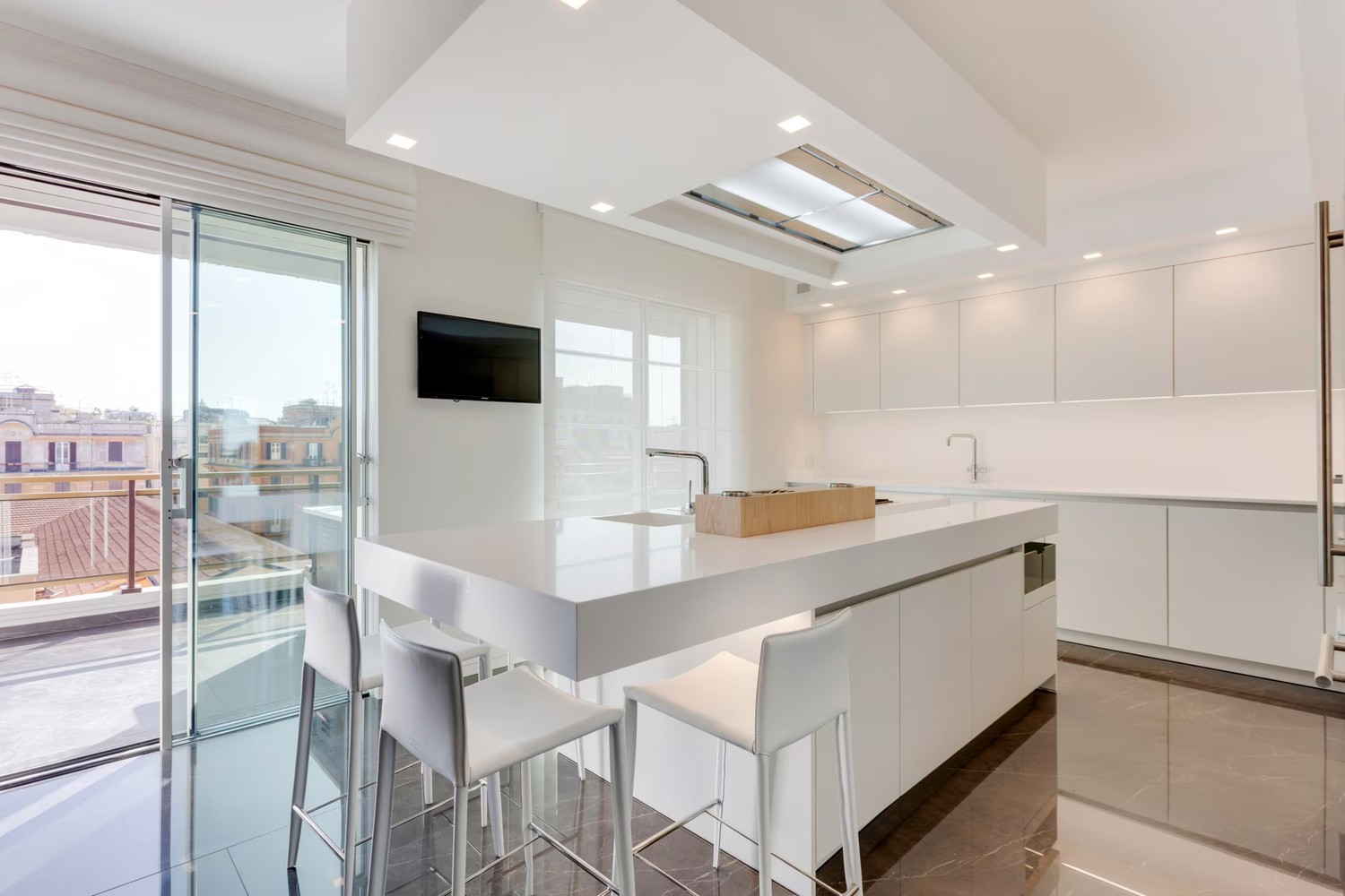 Minimalistyczna biała kuchnia z wyspą i oknem fot. Porcelanosa