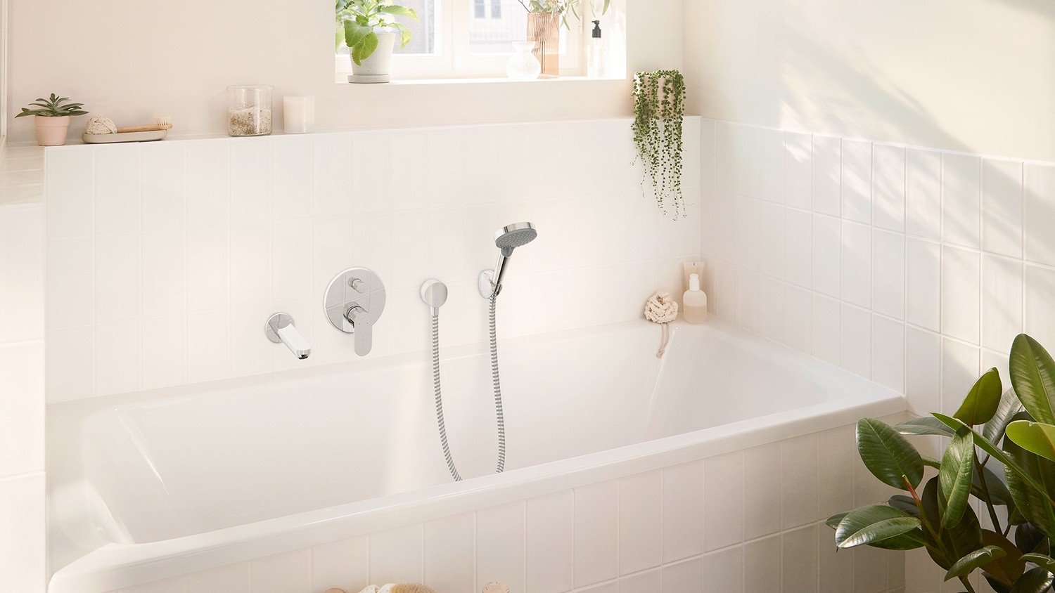 Biała wanna przy oknie z chromowaną baterią fot. Hansgrohe