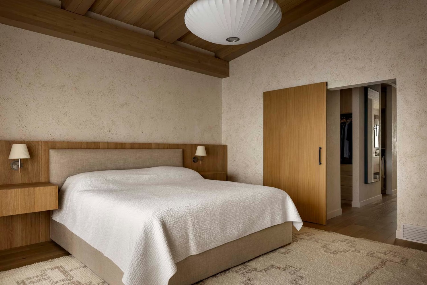 Japandi sypialnia z drewnianym łóżkiem i dywanem. fot. Porcelanosa