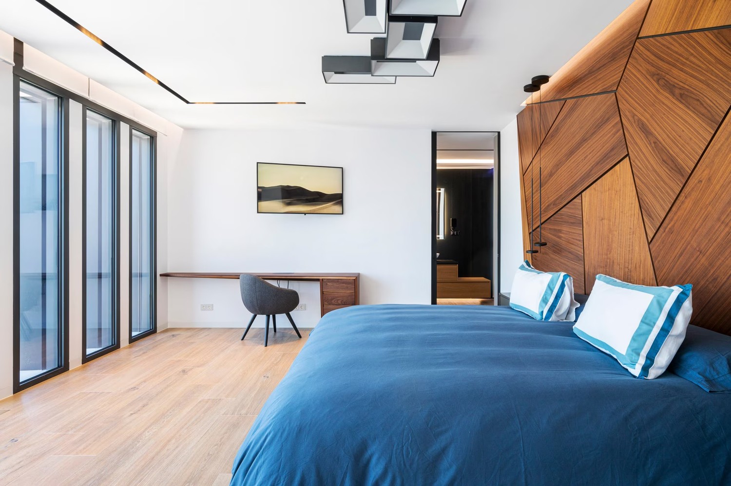 Minimalistyczna sypialnia z drewnianą ścianą i biurkiem. fot. Porcelanosa